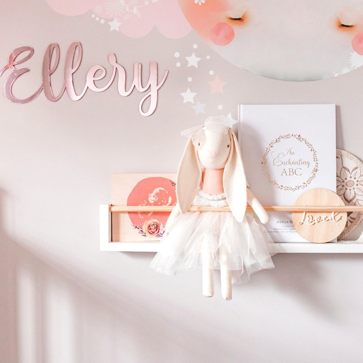 This is a white bookshelf with wooden peg across in a nursery room. The bookshelf has books , plush toy and accessories