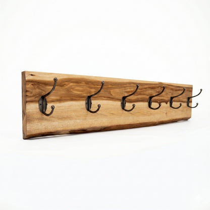 A clean product shot of a live-edge camphor laurel wood coat rack with six antique-style black double hooks, isolated at an angle against a seamless, solid white background to showcase the natural wood grain.