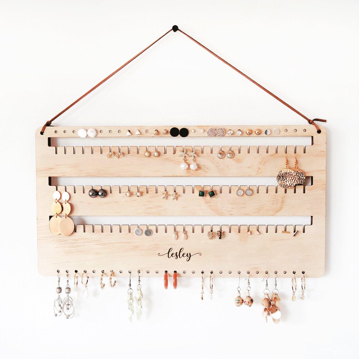 This is a personalised wall earring holder with leather string hanging on a screw. Stud, hook and dangling earrings are organised on this earring holder. A perfect gift for mum