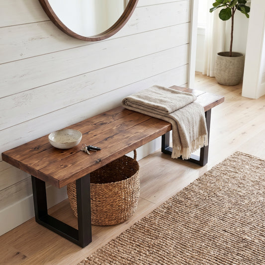 Rustic solid wood entryway bench with matte black industrial steel U-legs, styled with a beige fringed throw blanket, ceramic key bowl, and a woven storage basket on a textured jute runner rug.