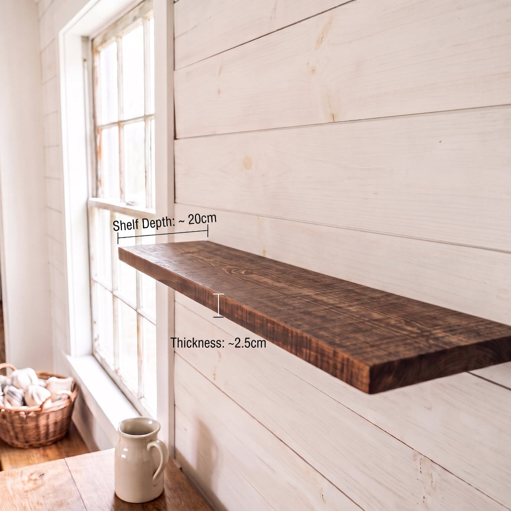 A floating dark wood shelf mounted on a white shiplap wall, with measurement labels indicating a depth of approximately 20cm and a thickness of approximately 2.5cm.